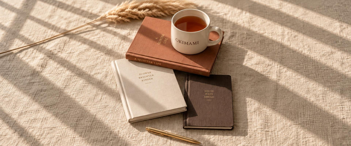 Hands writing in an OKIMAMI Motherhood OS planner with a gold pen
